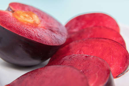 On a white saucer, a large plum, cut in half, with slices next to it. The pulp of red berries....