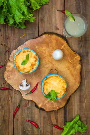 Pots with mushroom julienne on a wooden board, decorated with herbs. Julienne in cocotte with yellow...