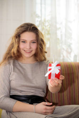 A young girl with long hair is tying a gift box for congratulations. Sits on the couch in the roomの写真素材