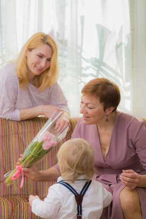 The kid congratulates mom and grandmother on the holiday, everyone hugs and laughs with happinessの写真素材