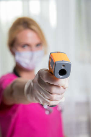 A girl doctor in a mask with an outstretched hand, a device for measuring temperature in her hand.の写真素材