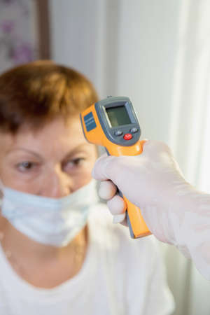 A female doctor measures the temperature of an adult woman with a laser device.の写真素材