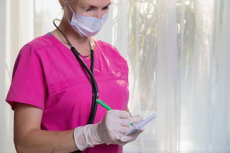 A girl doctor in a mask and gloves writes down the readings of the patients temperature and pressure...