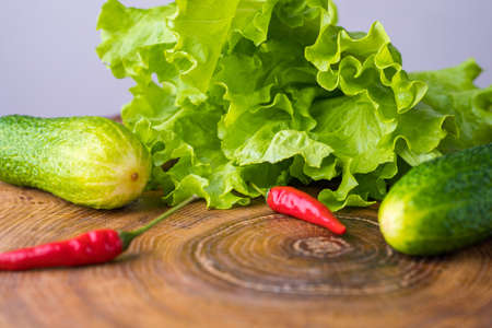 Fresh wholesome foods: green salad, cucumbers and red chili peppers lie on a cutting board. Healthy food concept.の写真素材