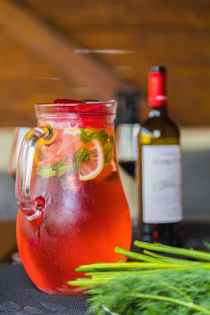 Lunch with a decanter of chilled red fruit drink with lemon wedges. A bottle of wine and herbs. Close-up.の写真素材