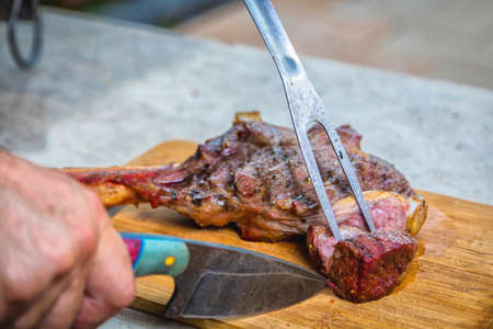 A man cuts cooked fried meat on a cutting board. Oven-baked meat for dinner.の写真素材