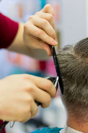 The hairdresser cuts the man's hair with a clipper and comb. Short men's haircut. Close-up.の写真素材