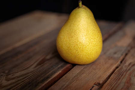 Juicy yellow pear on a wooden background from old boards in a low key.の写真素材