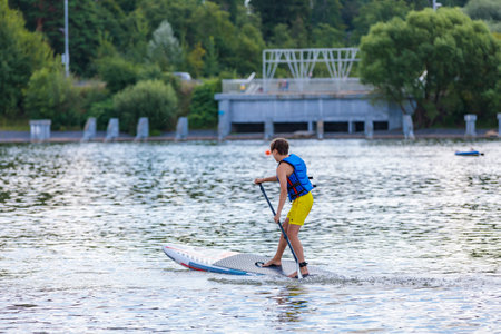 A child swims on a surfboard, pushing off with a paddle. Paddleboarding.のeditorial素材