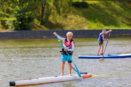 A child swims on a surfboard, pushing off with a paddle. Paddleboarding.のeditorial素材