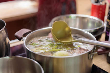 A metal saucepan filled with boiling vegetable and meat broth. There is a scoop in the broth.の写真素材