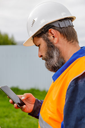 A civil engineer looks at a mobile phone. A bearded man is looking for information on his mobile phoneの写真素材