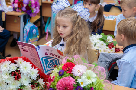 The first grader sits at her desk in the classroom and reads the alphabet. A girl with white bows...