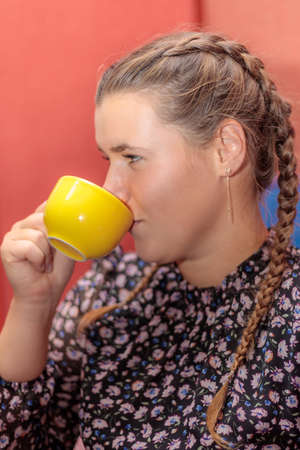Cheerful girl drinks coffee from a yellow mug. Young girl with pigtails drinks a drink.の写真素材