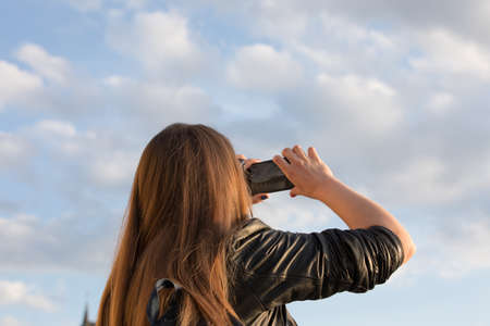 Girl tourist takes pictures of the sky with fluffy clouds on a mobile phoneの写真素材
