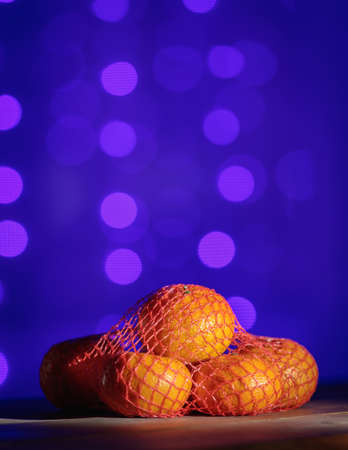 Mesh with tangerines on the background of Christmas lights. Blue bokeh.の写真素材