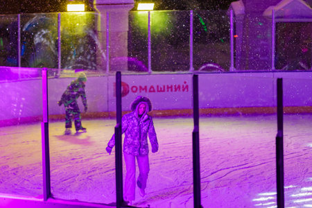 People skate in the evening on a lighted ice rink. A blizzard is raging and snow is falling. Zelenograd, Russia 28.01.2022.のeditorial素材
