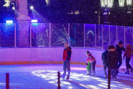 People skate in the evening on a lighted ice rink. A blizzard is raging and snow is falling....