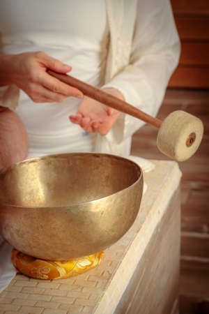 A woman performs Tibetan singing bowl therapy with a man lying under a white sheet. Relaxing meditation.の写真素材