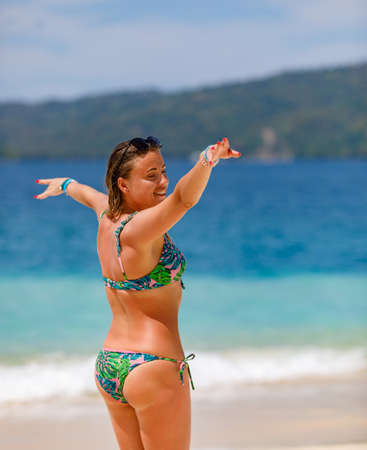 A young girl in a green bathing suit stands by the sea and laughs with her arms outstretched. High quality photoの写真素材