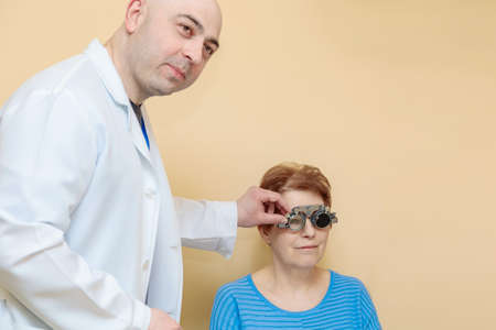 A male optometrist checks the eyesight of an adult woman with a trial frame.