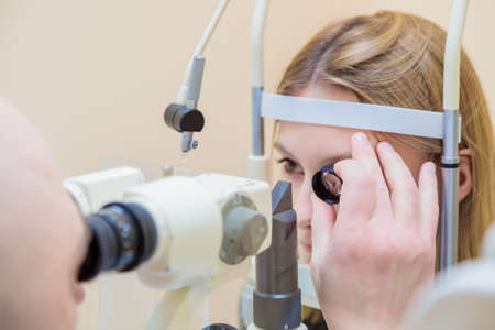 A male ophthalmologist checks the eyesight of a young girl using a modern device with a light beam.の写真素材