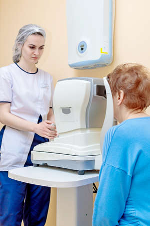A girl optometrist examines the eyes of a patient using special modern equipment.