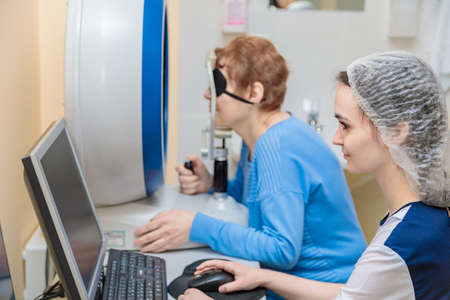 A girl optometrist examines the eyes of a patient using special modern equipment.