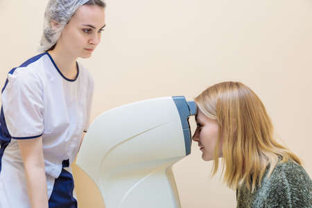 A girl optometrist examines the eyes of a patient using special modern equipment.