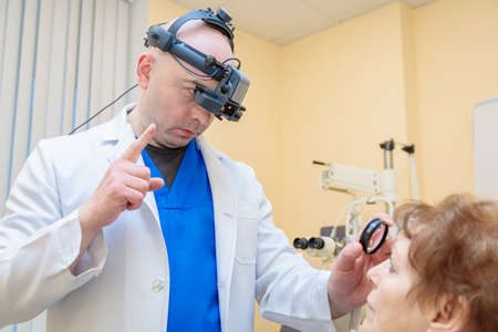 A male ophthalmologist checks the eyesight of an adult woman with a binocular ophthalmoscope.