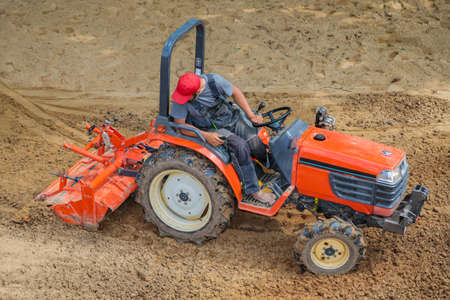 A farmer on a mini tractor loosens the soil for the lawn. Land cultivation, surface leveling.