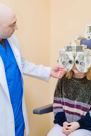 A male ophthalmologist checks a girl's eyesight using a phoropter. vision treatment.の写真素材