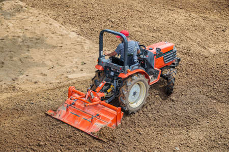 A farmer on a mini tractor loosens the soil for the lawn. Land cultivation, surface levelingの写真素材