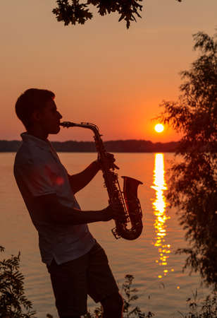 A young guy plays the saxophone in the evening at sunset.の写真素材