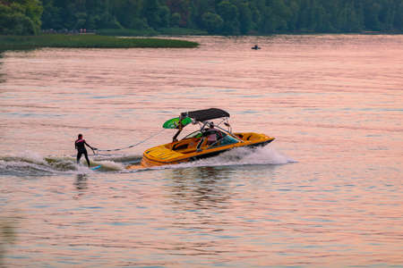 A boat pulls a person over the waves on a wakeboard. Wakeboarding at sunset.の写真素材