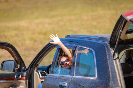 Smiling happy girl waving from the car window while traveling in the mountainsの写真素材