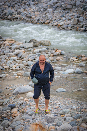 A man stands by a mountain river and holds a stone in his handsの写真素材