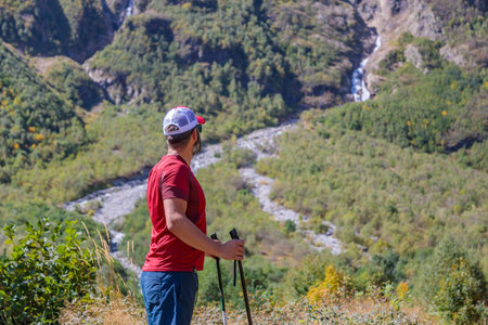 A hiker with canes looks into the distance on a path in the mountains to the waterfalls