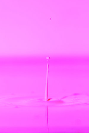 A drop falls into a thick liquid with a pink background. Abstract colorful background.