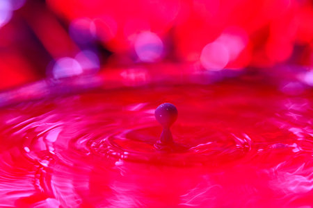 A drop falls into a dense liquid with a red background. abstract colorful backgroundの写真素材