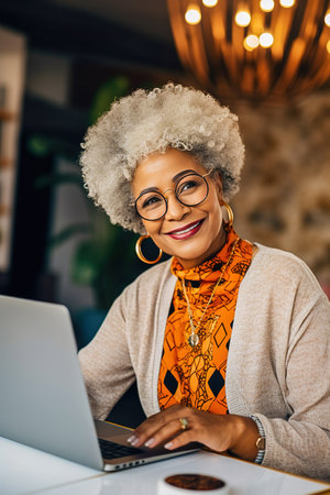 A happily retired African-American woman with gray hair works at her computer. High quality photoの素材