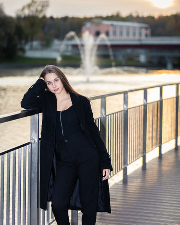 Portrait of a girl on a bridge near a pond in a city park against the backdrop of fountainsの写真素材