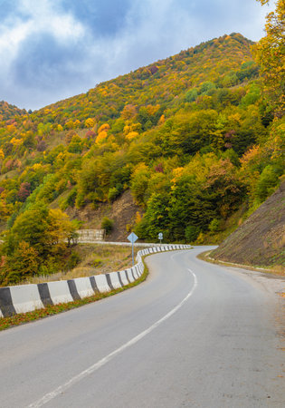 Winding road to the mountains. Sunny autumn in the mountains covered with bright colorful trees