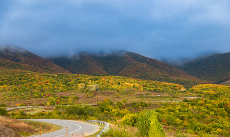 Winding road to the mountains. Sunny autumn in the mountains covered with bright colorful trees