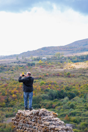 Man taking pictures of mountains while standing on the ruins of a wallの写真素材