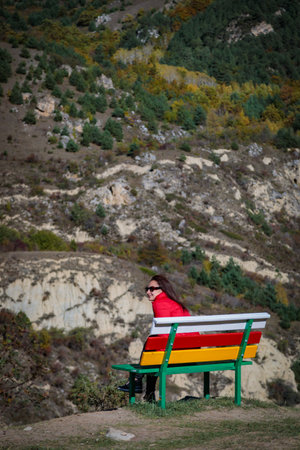 Young woman resting enjoying the view of the mountains while sitting on a wooden benchの写真素材
