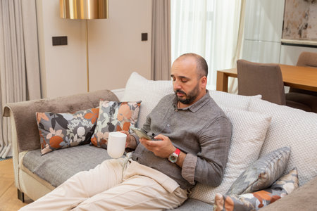 Relax on the couch with your smartphone and a drink.の写真素材