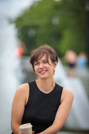 Smiling lady enjoying the aroma of coffee surrounded by the sounds of a fountain and the greenery of a secluded parkの写真素材