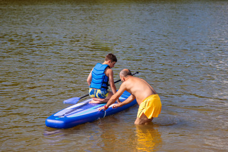 Family time on the water: A father teaches stand-up paddle boarding skills to his son.の写真素材