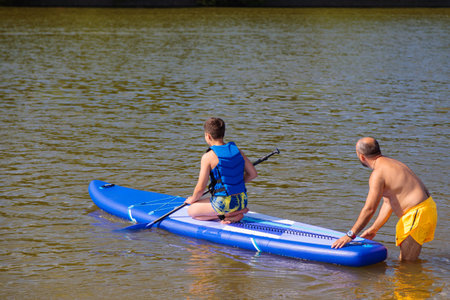 Family time on the water: A father teaches stand-up paddle boarding skills to his son.の写真素材